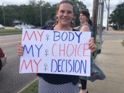 Activist protest on sidewalk outside a fake clinic in Columbia MO, holding signs with information about medication abortion and repro justice