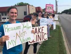 Activist protest on sidewalk outside a fake clinic in Columbia MO, holding signs with information about medication abortion and repro justice