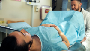 Image Courtesy of the Gender Spectrum Collective. [Image Description: a genderqueer person in a hospital gown receiving a pelvic exam]