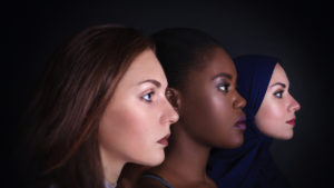 Three women portrait. Caucasian and afro-american women posing in studio over black background.