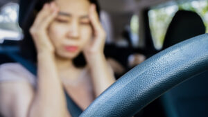 fatigued Asian woman suffering from headache migraine while driving a car